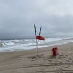 Red warning flag snapping in the wind on the Atlantic coast, reflecting stormy energy and the insistence to write.