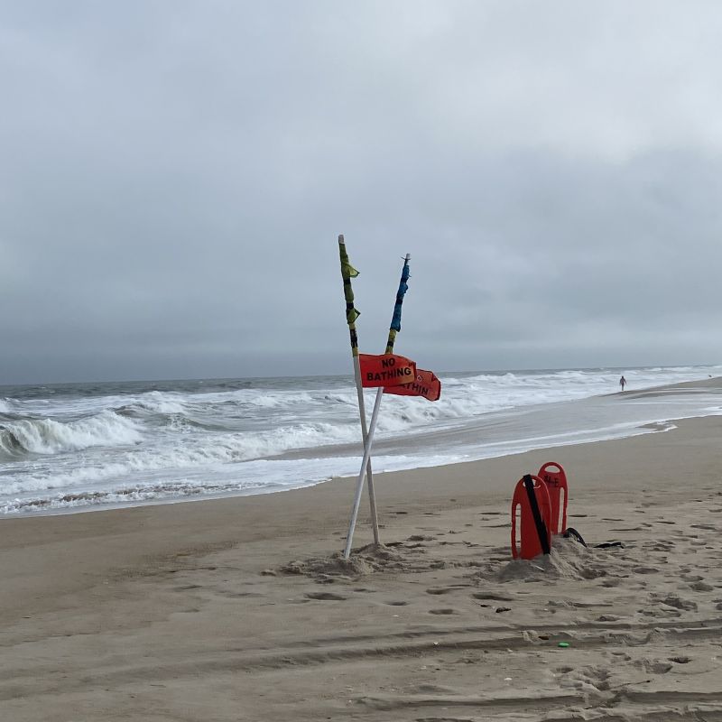 Red warning flag snapping in the wind on the Atlantic coast, reflecting stormy energy and the insistence to write.